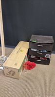 Photo showing the boxed 6.5-foot pre-lit flocked Frisco Christmas tree and stacked Sterlite drawers, with loose holiday decorations including a glass vase and red artificial flower visible at the base