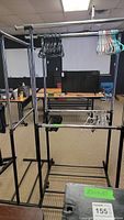 Three metal clothes racks with horizontal bars, some with clothes hangers in various colors, placed in a room with carpeted floor and furniture in the background.