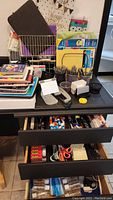 Wide view of desk with various office supplies including organizers, notepads, scissors, glue sticks, markers, and storage drawers open showing more supplies.
