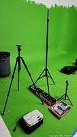 Wide view of all items against green backdrop: projector, tripods, light stand, kit in box