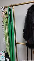 Brass colored adjustable clothing rack with green and black clothes hanging, shown from side angle