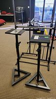 Pair of two black metal Pro Line speaker stands with triangular bases, rectangular tops, and adjustable heights