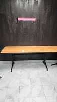Full view of rectangular melamine top office table against black wall with tiled floor.