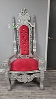 Front view of ornate throne chair with silver-painted carved wood frame and red velvet seat and back