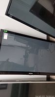 Photo showing Samsung 50 inch TV screen with black bezel and Samsung logo on bottom center. Screen is turned off and reflective.