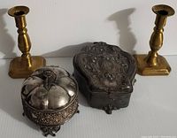 Photo showing the full set of four items including two brass candlestick holders and two silver plated ornamental vanity boxes.