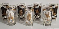 Front view showing seven drinking glasses arranged in a row with detailed white and black prints featuring historic American symbols and gold accents.