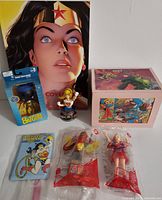 Full view of all 7 items including DC Comics Cover Girls book, Batgirl figure in box, Supergirl bust, Wonder Woman light switch plate, custom Supergirl trinket box, and two McDonald's superhero figures in packaging