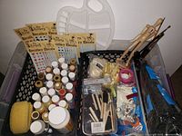 Overview of the art supplies in baskets, showing paints, brushes, decals, palette, sponge, and craft tools.