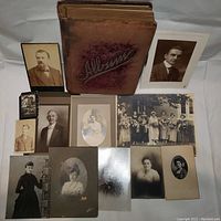 Full lot showing vintage Victorian photo album with miscellaneous Victorian-era photographs surrounding it on a white surface