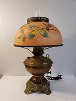 Front side view of the antique electric converted oil lamp showing painted floral glass shade, ornate brass base, and visible power cord.