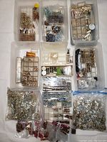 Overview of all jewelry supplies including gemstones, pearls, and settings organized in plastic boxes and bags.