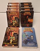 Front view of the ten Tomb Raider collectible card game decks. Five 'Trapped in the Tombs' decks, four 'Into the Caves' decks, and one 'Pacific Peril' deck visible. One 'Trapped in the Tombs' deck is open while others appear sealed.