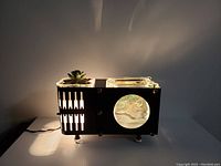 Lamp illuminated showing light projection from vertical slits and mural window with scenic landscape.