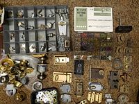 Top-down view showing spread of vintage locks, latches, doorknobs, lock cylinders with keys, and miscellaneous door hardware pieces along with the keying kit in its plastic box containing pins and springs.