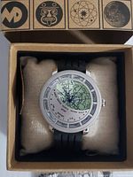 Top-down image of watch in packaging showing large dial displaying northern hemisphere constellations with black rubber band.