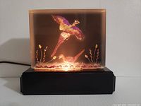Front view of lamp lit showing illuminated pheasant birds inside translucent rectangular panel on black base.