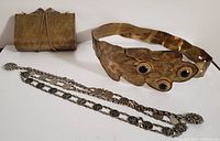 Photo showing the black and silver belt with oriental girl circular designs, flowered ends with chain links, the brass-colored metal belt with decorative circular elements, and the vintage metal peacock clasp purse with chain and engravings.