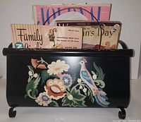 Black curved metal vintage magazine rack with floral and bird decoration holding various vintage magazines including Woman's Day, Family Circle, and Journal Magazine.