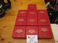 Ten sealed red boxes of Hummel Gold Christmas Ornaments arranged in grid