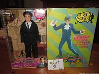Front view of the lot showing packaged Patrick Dempsey doll on left and Austin Powers cold cast statue box on right, sign with lot number in center.