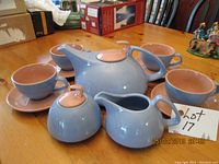 Full set view showing teapot, creamer, sugar bowl, four cups and saucers with blue and peach colors, arranged on wooden table.
