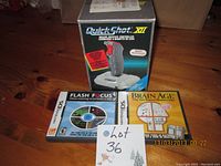 Photo showing QuickShot XII Joystick in box with Nintendo DS games Flash Focus and Brain Age, with a lot number card on wooden floor.