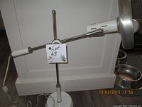 Full view of the articulating desk light on its stand showing the solid round base, adjustable chrome arms, and white handle at the end.