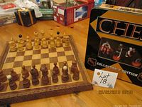 Traditional wooden chess set displayed on a table, showing the chessboard with carved wood and chess pieces arranged for play. Tin case for NHL chess set is visible beside it.