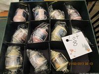 Box containing 11 individually boxed Thomas Kinkade collectible Christmas bulbs, each wrapped in protective plastic.