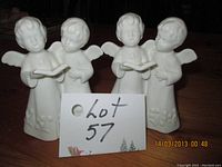 Front view of the two ceramic angel candle holders, showing four angels with open books and floral detail, white glossy finish.