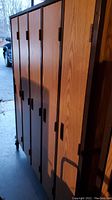 Side view of five wood finish lockers with black trim and vertical doors with handles, showing the full height of about 4.5 feet.