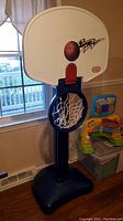 Photo of first basketball hoop, white backboard with basketball graphic, blue hoop, white nylon net, attached to black weighted base