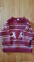 Burgundy knit sweater with white and pink geometric and reindeer pattern laid flat on wooden floor