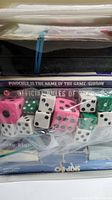 Close-up view of Pinochle by Gibson box, Official Rules of Card Games, assorted pink, white, and green dice in clear plastic bag.