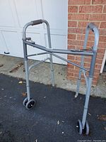 Side angle view of silver metal folding walker showing front wheels, padded hand grips, and two-button folding mechanism.