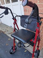 Side angled view of red Drive Medical fold-up rollator walker showing padded seat, ergonomic handlebars with brakes, front bag, and wheels.