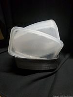 Photo showing stack of multiple translucent rectangular containers with white lids.