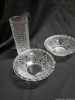 Three glassware items on a black background: one textured tall vase and two etched candy dishes.