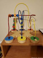 Full view of the wooden bead maze toy on a shelf, showing colorful metal loops with beads.