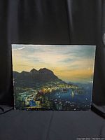 Front view of cityscape oil painting depicting buildings, water, mountains at dusk under a gradient sky.