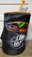 Collapsible black toy storage bag with orange trim containing soft toys