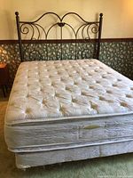 View of full bed with tufted mattress on box spring and metal frame with wheels