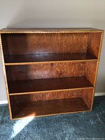 Photo of wooden bookshelf showing three shelves and decorative edge.
