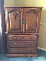Full frontal photo showing the entire wooden cabinet with two upper doors and three lower drawers, brass hardware visible, natural wood finish.