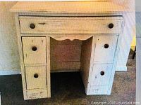 Front view of the distressed white wooden desk showing the multiple drawers and overall construction.