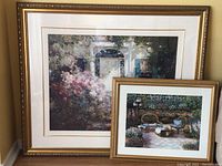 Photo of two framed art pieces featuring garden scenes with floral and furniture elements.