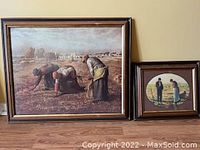 Framed art prints grouped together on a floor showing both pieces side by side. Larger rectangular print shows three women harvesting crops, smaller oval print shows a man and woman outdoors.