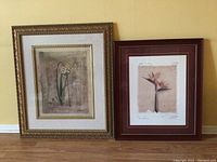 Two framed floral art prints, one larger in gold frame and one smaller in dark wooden frame, leaning against a wall.