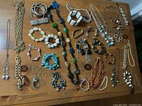 Photo of assorted costume jewelry laid out on wooden surface with necklaces, bracelets, and earrings visible